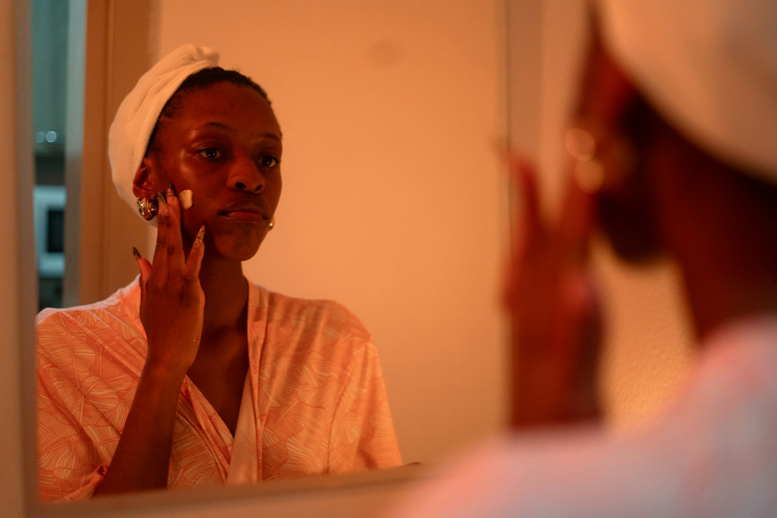 Woman applying face cream in front of a mirror in warm evening light